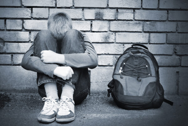 Homeless youth sitting on curb with backpack, at risk of exploitation
